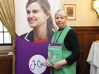 Su Moore standing with her report infront of a large sign reading Jo Cox